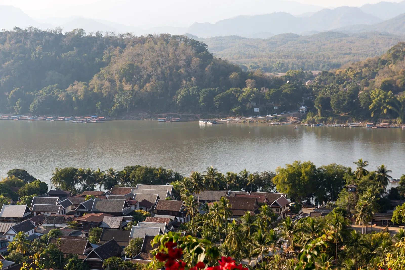 Aerial view from Phousi Hill over Luang Prabang's rooftops, the Mekong River, and forested mountains beyond.