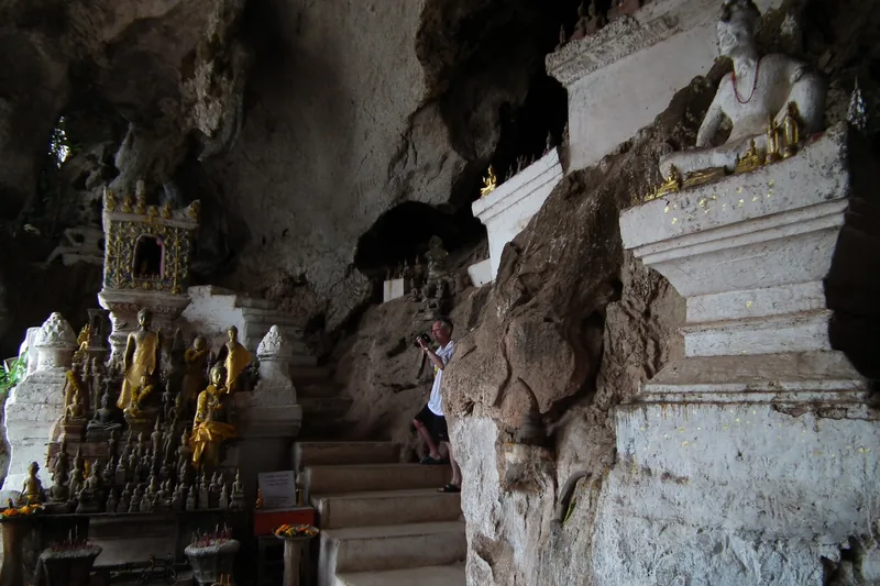 A visitor photographs rows of small Buddha statues and shrines inside the Pak Ou Caves near Luang Prabang.