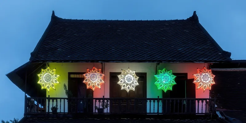 Colorful star-shaped lanterns light up a traditional balcony at dusk in Luang Prabang.