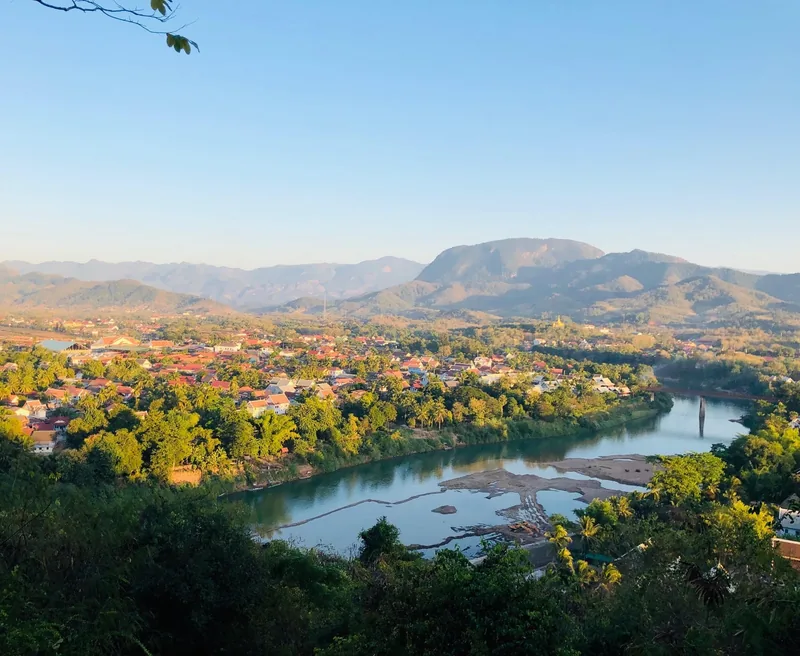 Elevated view of Luang Prabang town nestled along the Mekong River with mountains behind at golden hour