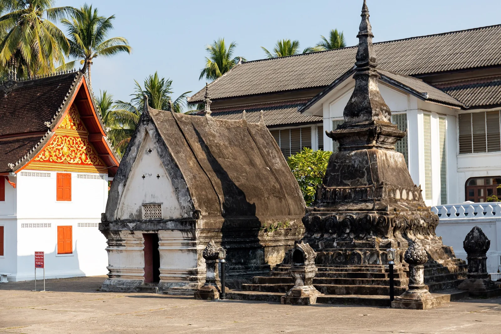 A weathered stupa and small chapel stand before white temple buildings in Luang Prabang. A weathered stupa and small chapel stand before white temple buildings in Luang Prabang.