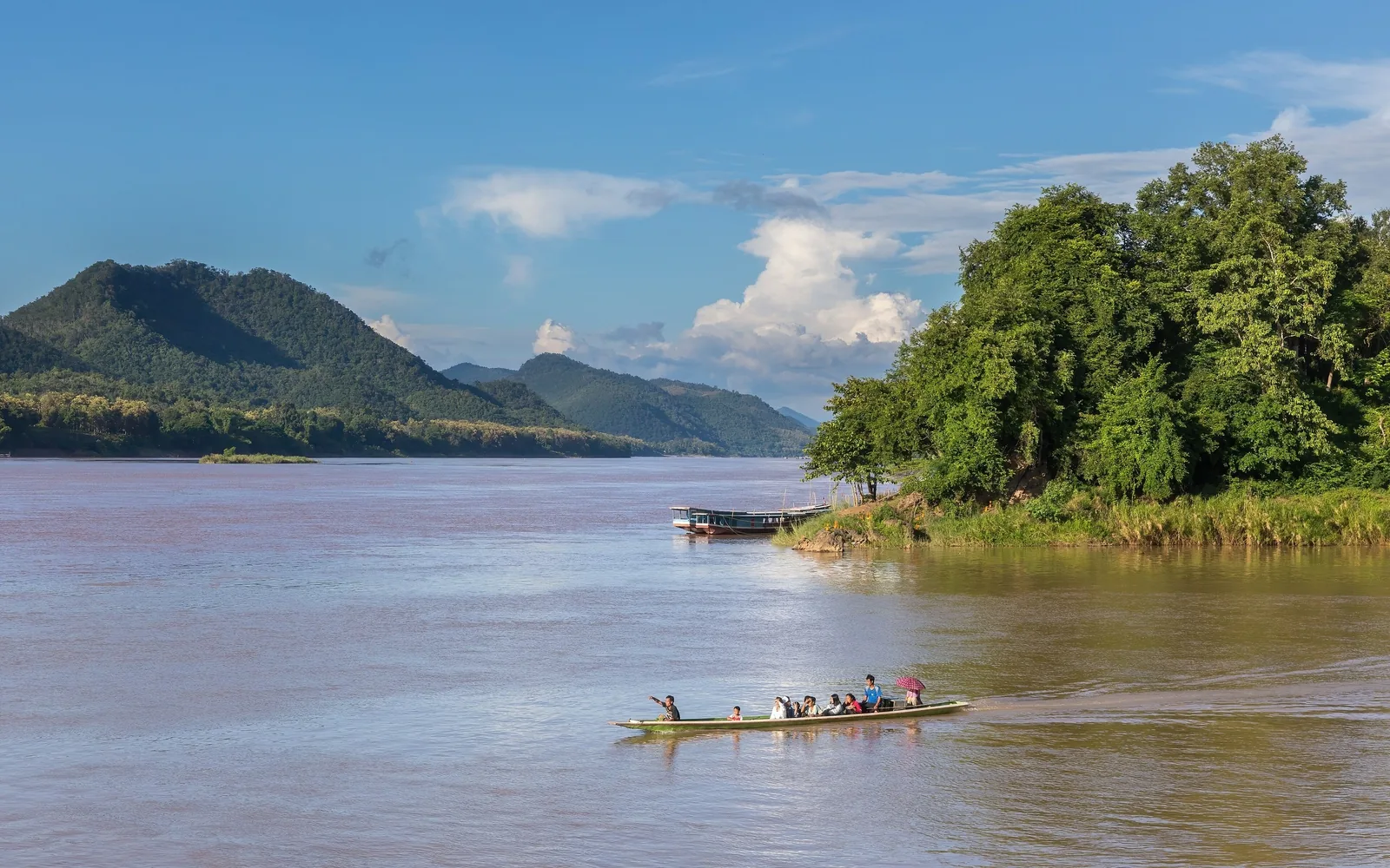 A long-tail boat carries passengers across the Mekong River near forested hills in Luang Prabang.