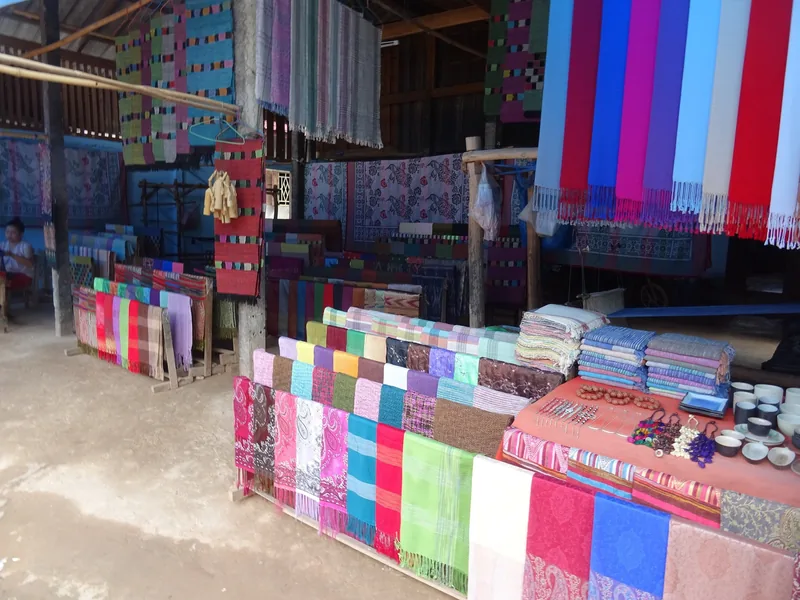Colorful handwoven textiles and scarves hang for sale at a village weaving workshop near Luang Prabang.
