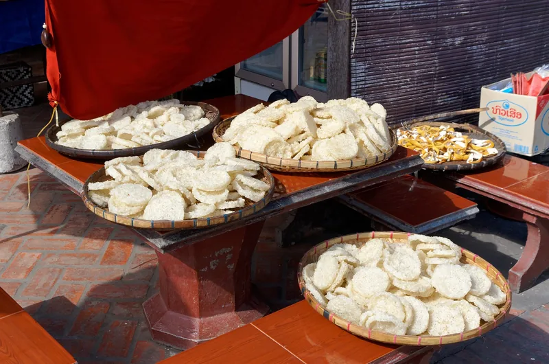 Woven baskets of dried rice cakes drying in the sun on a wooden table in Luang Prabang, Laos.