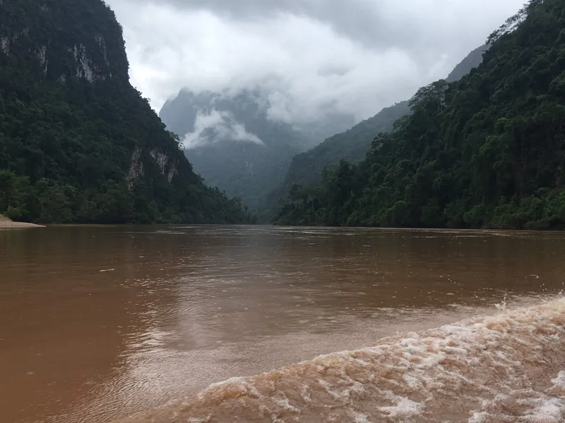 Muddy river flows between misty limestone cliffs and jungle near Nong Khiaw, Laos.