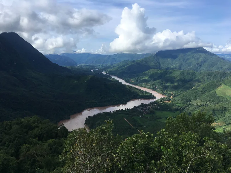 A muddy river winds through green mountain valleys as seen from Pha Daeng Peak viewpoint in Nong Khiaw, Laos.