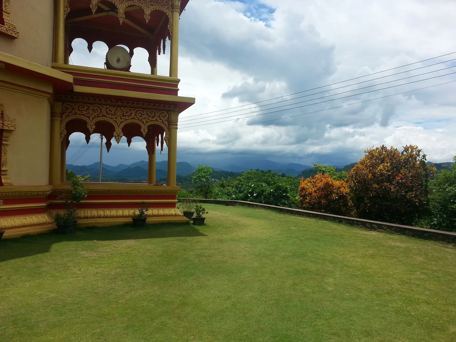 A gilded temple pavilion with a drum overlooks a grassy hillside and misty mountains in Luang Prabang.
