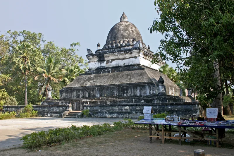 A weathered dome-shaped stupa stands beside a market stall at Wat Visoun temple in Luang Prabang.