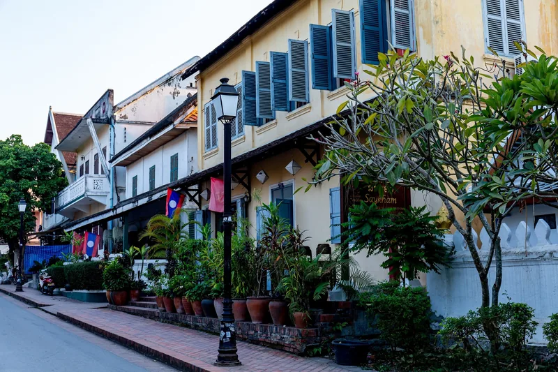 French colonial-style buildings line a quiet street with potted plants in Luang Prabang, Laos.