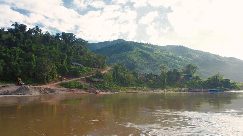Excavators work along a dirt road beside the muddy Mekong River near forested hills between Luang Prabang and Pakbeng, Laos.