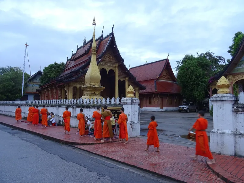Buddhist monks in orange robes collect alms outside a temple in Luang Prabang, Laos.