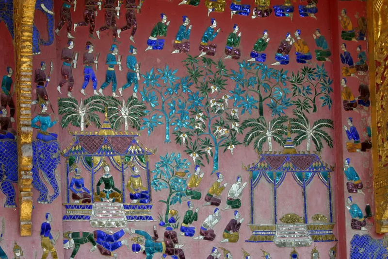 Colorful glass mosaic mural depicting figures, pavilions and trees on a temple wall in Luang Prabang.