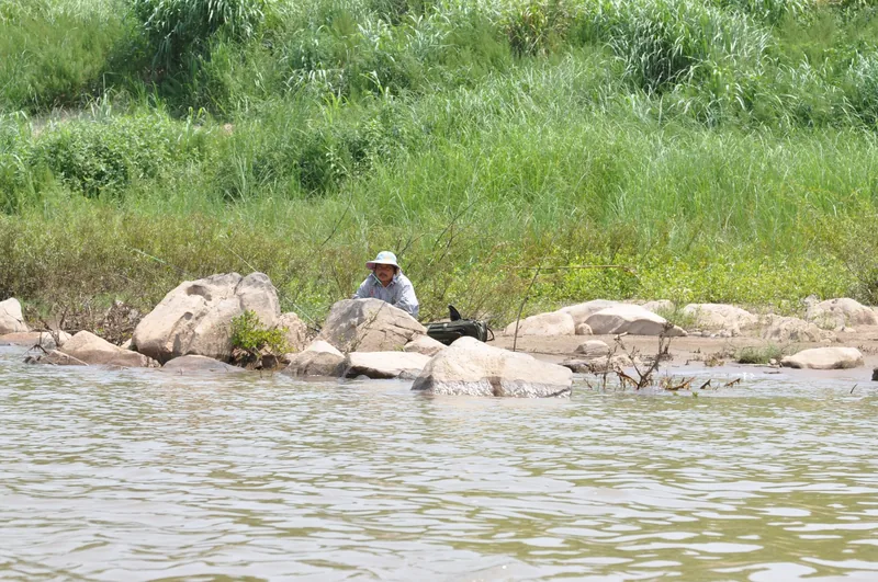A man in a sun hat fishes among rocks along the Mekong riverbank near Luang Prabang.