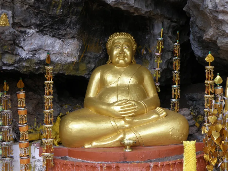 A golden seated Buddha statue rests inside a rocky cave shrine at Wat Tham Mo Thayaram near Luang Prabang.