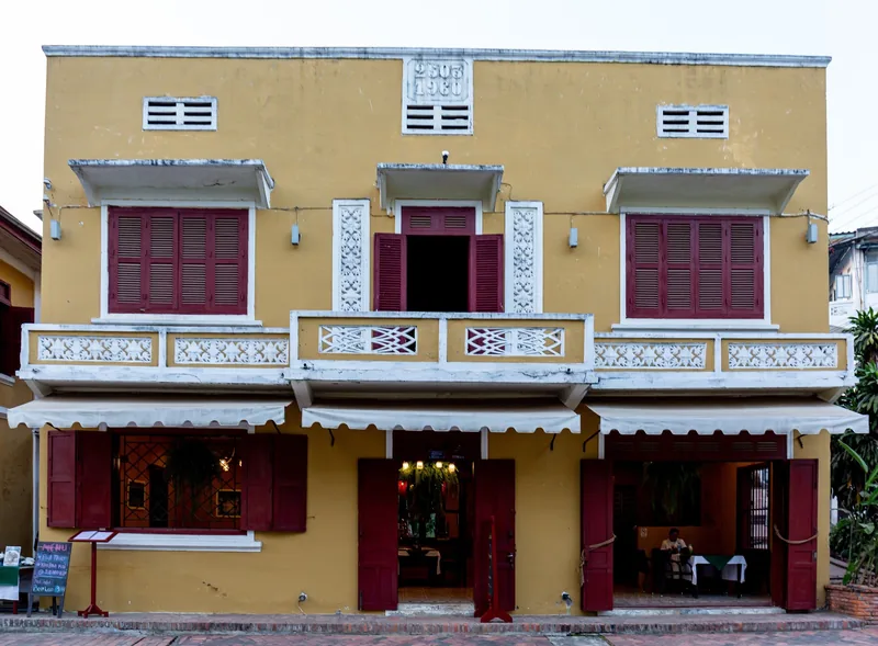 A colonial-era yellow building with red shutters lines Sisavangvong Road in Luang Prabang.