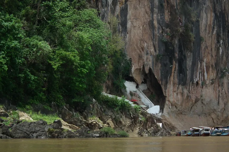 Boats moor below the limestone cliff entrance to Pak Ou Caves along the Mekong River near Luang Prabang.