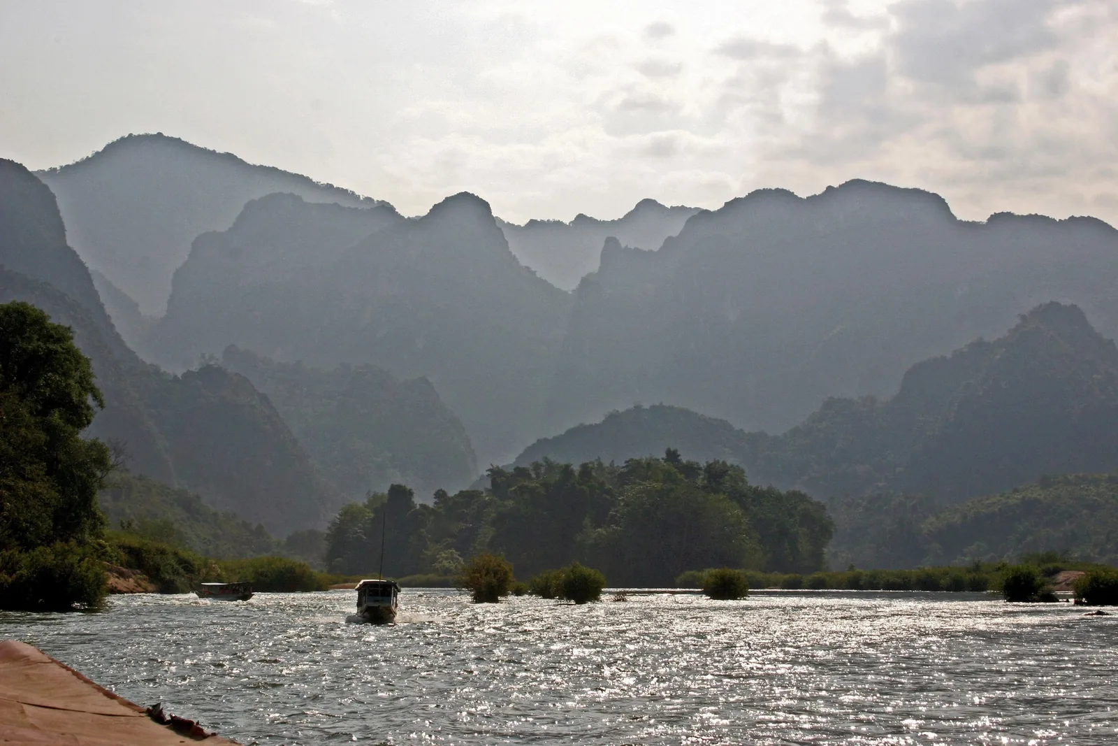 A small boat glides along the Nam Ou river beneath dramatic karst mountains near Luang Prabang.