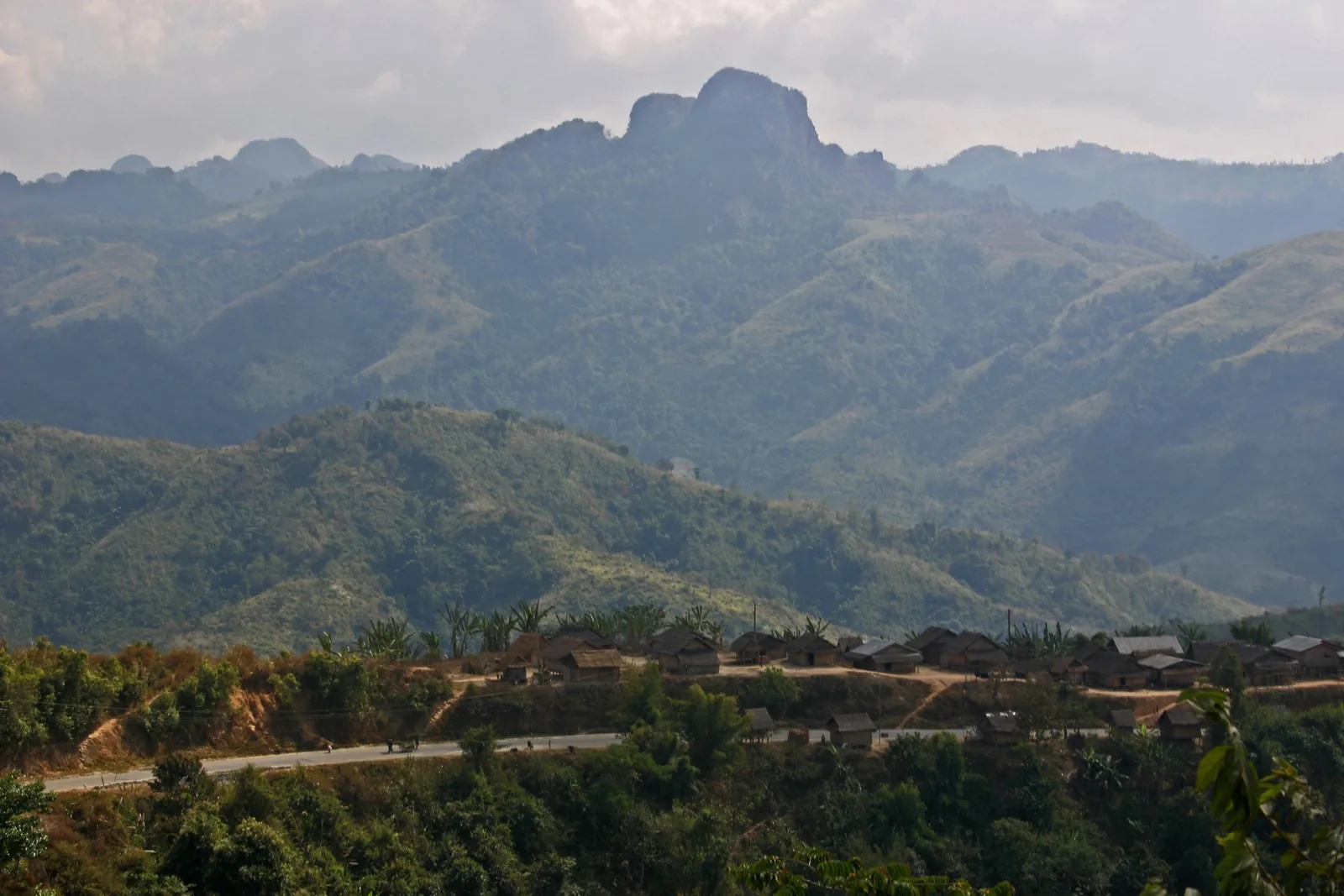 A small village of thatched huts sits along a mountain road amid layered green ridges near Luang Prabang. A small village of thatched huts sits along a mountain road amid layered green ridges near Luang Prabang.
