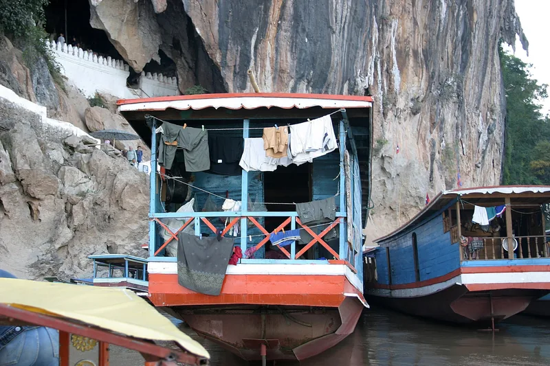 Wooden riverboats with laundry drying moor below the limestone cliffs of Pak Ou Caves near Luang Prabang.