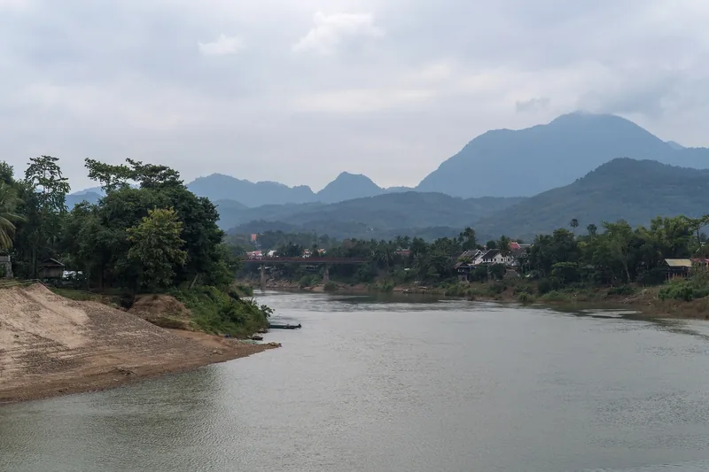 A calm river winds past sandy banks and forested hills toward misty mountains in Luang Prabang. A calm river winds past sandy banks and forested hills toward misty mountains in Luang Prabang.