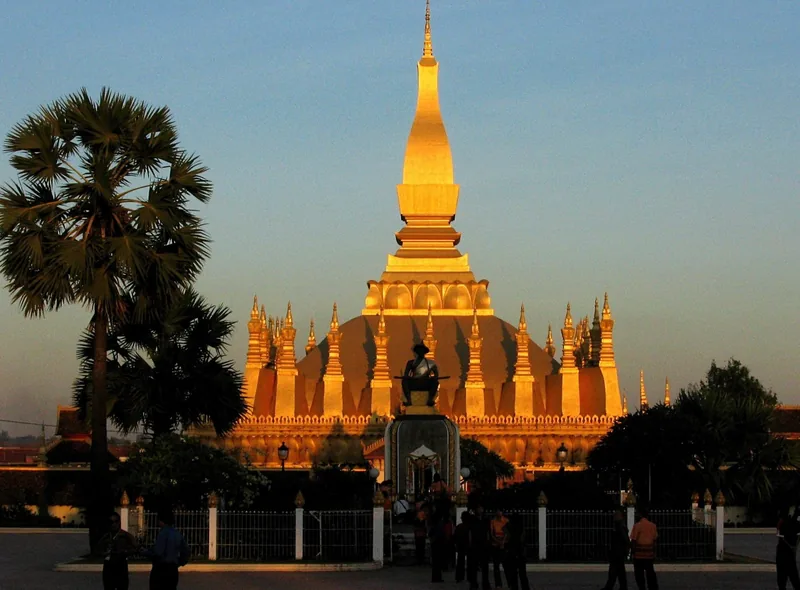 Golden spires of Pha That Luang stupa glow at sunset in Vientiane, framed by a palm tree. Golden spires of Pha That Luang stupa glow at sunset in Vientiane, framed by a palm tree.