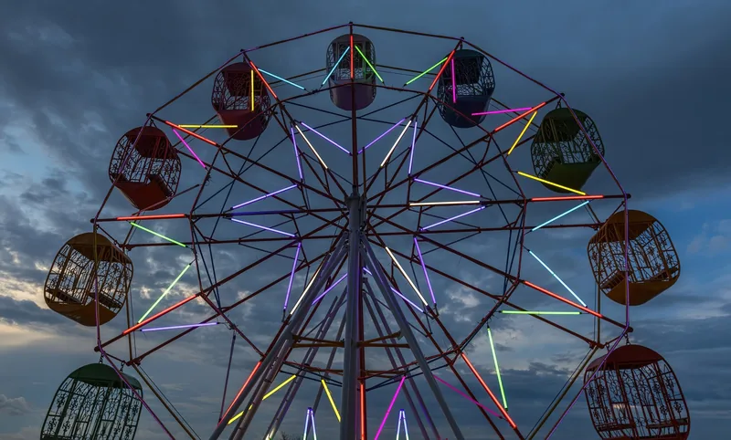 A colorful illuminated ferris wheel glows against a dusky cloudy sky in Vientiane. A colorful illuminated ferris wheel glows against a dusky cloudy sky in Vientiane.