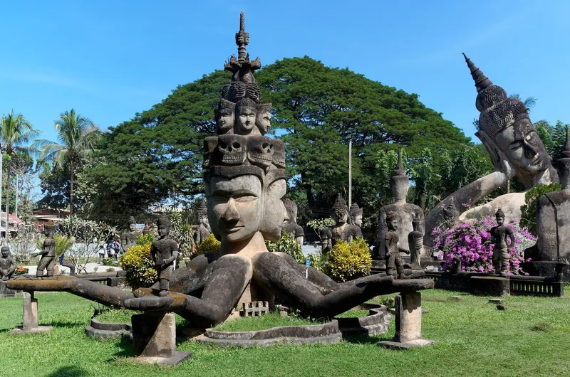 Multi-headed concrete statue and other Buddhist sculptures in Buddha Park, Vientiane, under a clear blue sky. Multi-headed concrete statue and other Buddhist sculptures in Buddha Park, Vientiane, under a clear blue sky.