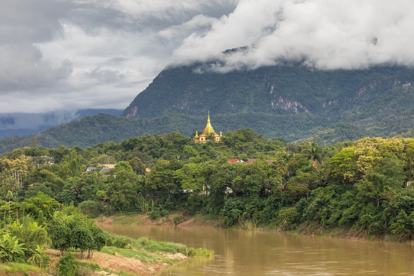 A golden stupa of Wat Pa Phon Phao rises above the treeline overlooking the Nam Khan River in Luang Prabang, with misty. A golden stupa of Wat Pa Phon Phao rises above the treeline overlooking the Nam Khan River in Luang Prabang, with misty.